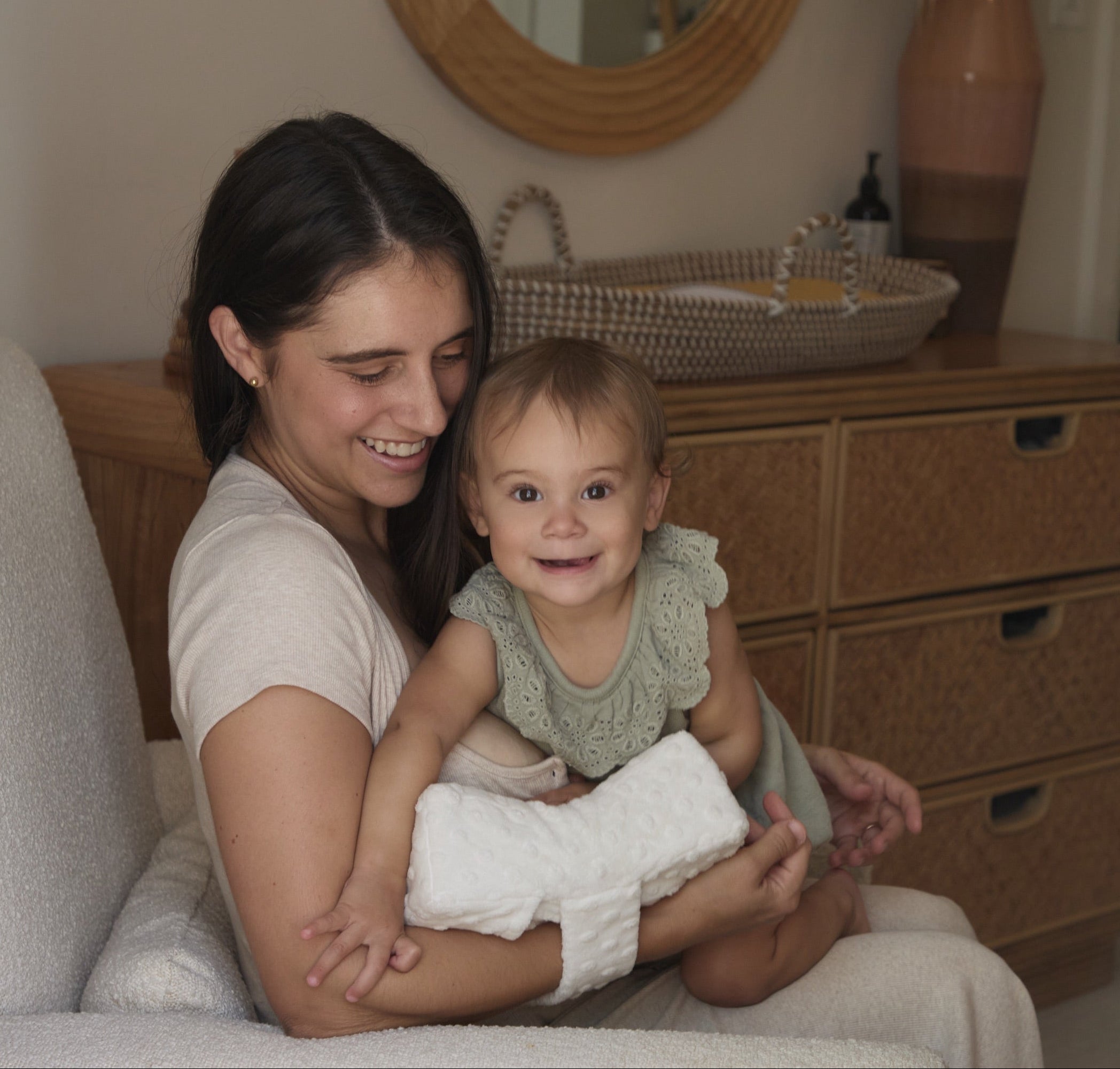 Woman holding a baby in a room with a dresser and mirror.