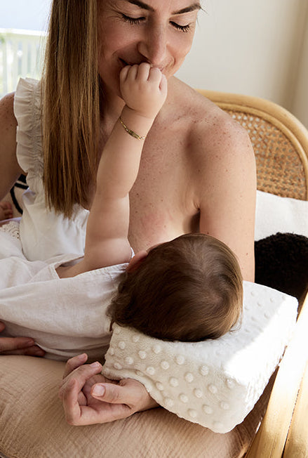 Woman holding a baby with bowroo nursing pillow on a wooden chair.